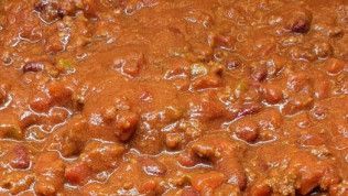 A close up of a bowl of chili with meat and beans.