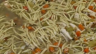 A close up of a pot of chicken noodle soup with carrots and celery.
