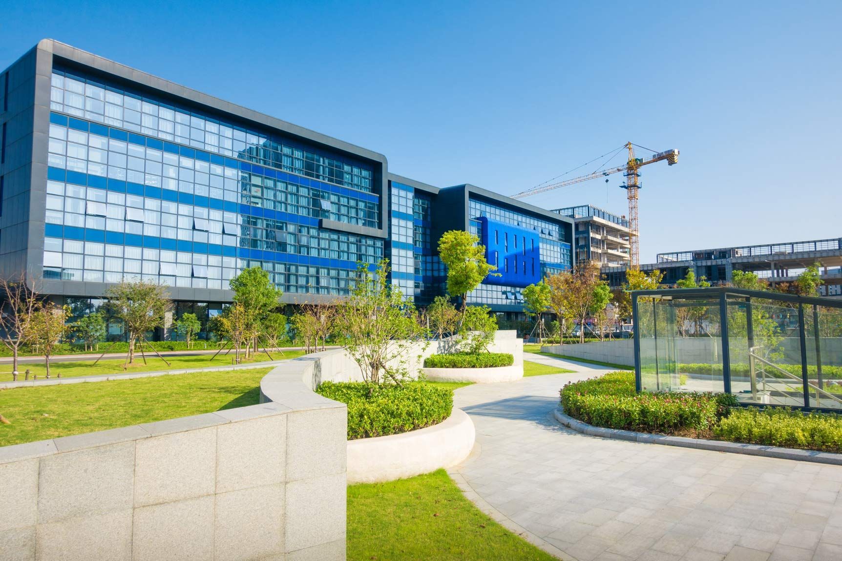 Modern office building with blue glass windows, green lawn, trees, and walking paths.