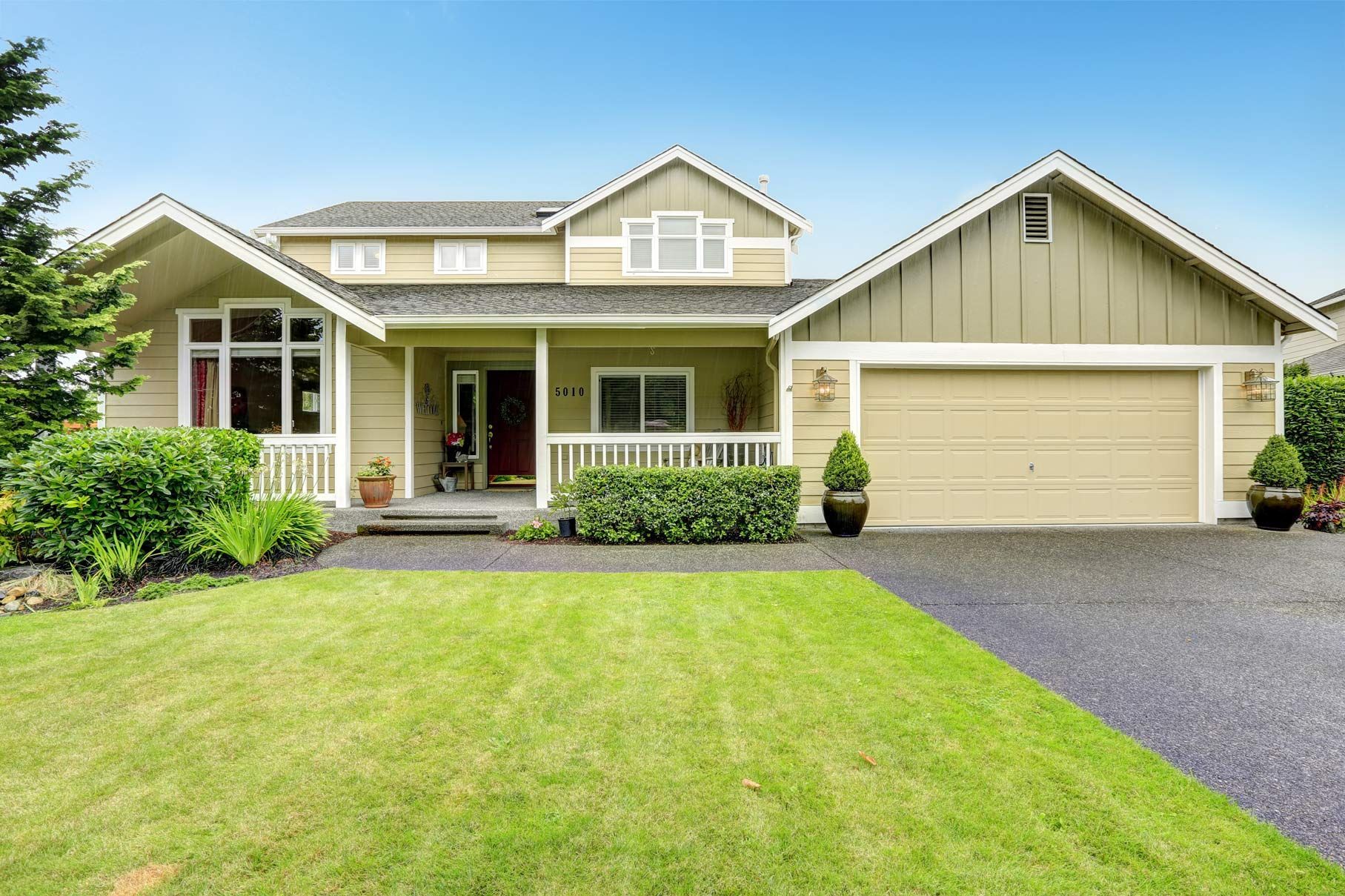 Beige two-story house with green lawn, driveway, porch, and attached garage under a blue sky.