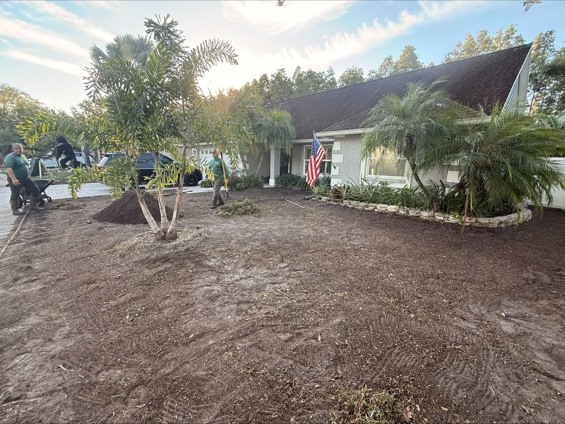 Landscapers mulching a front yard with a house in the background.