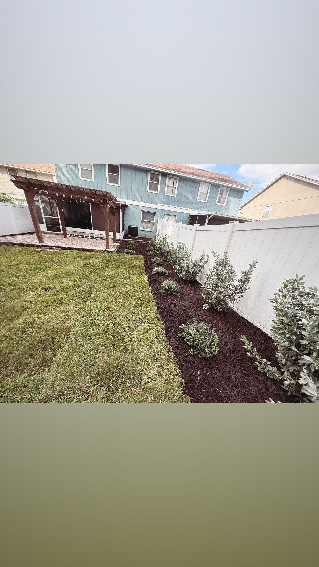 Backyard with lawn, flowerbed, white fence, and a wooden pergola on a deck.