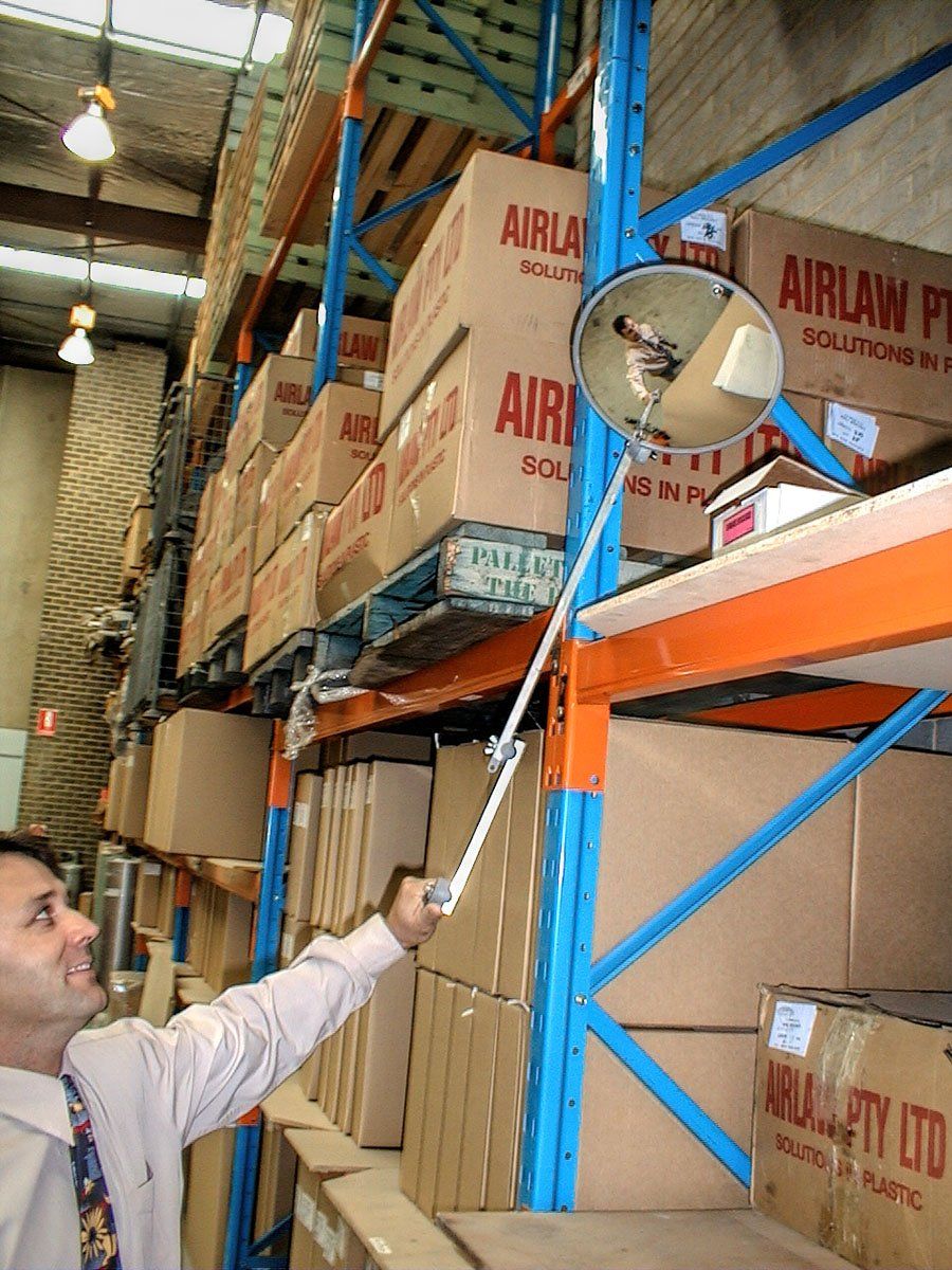 Man using an inspection mirror to see high shelving in a warehouse