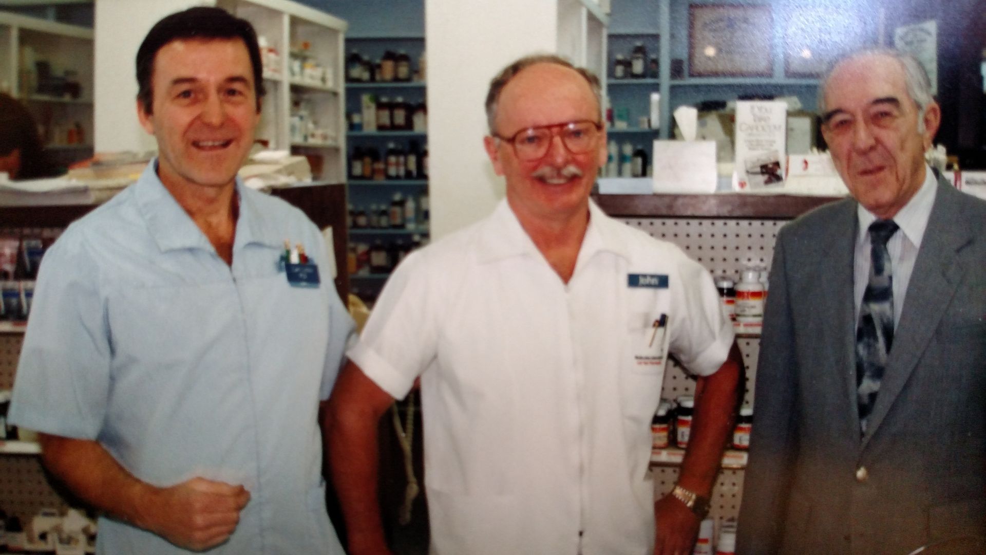 Three men are posing for a picture in a pharmacy