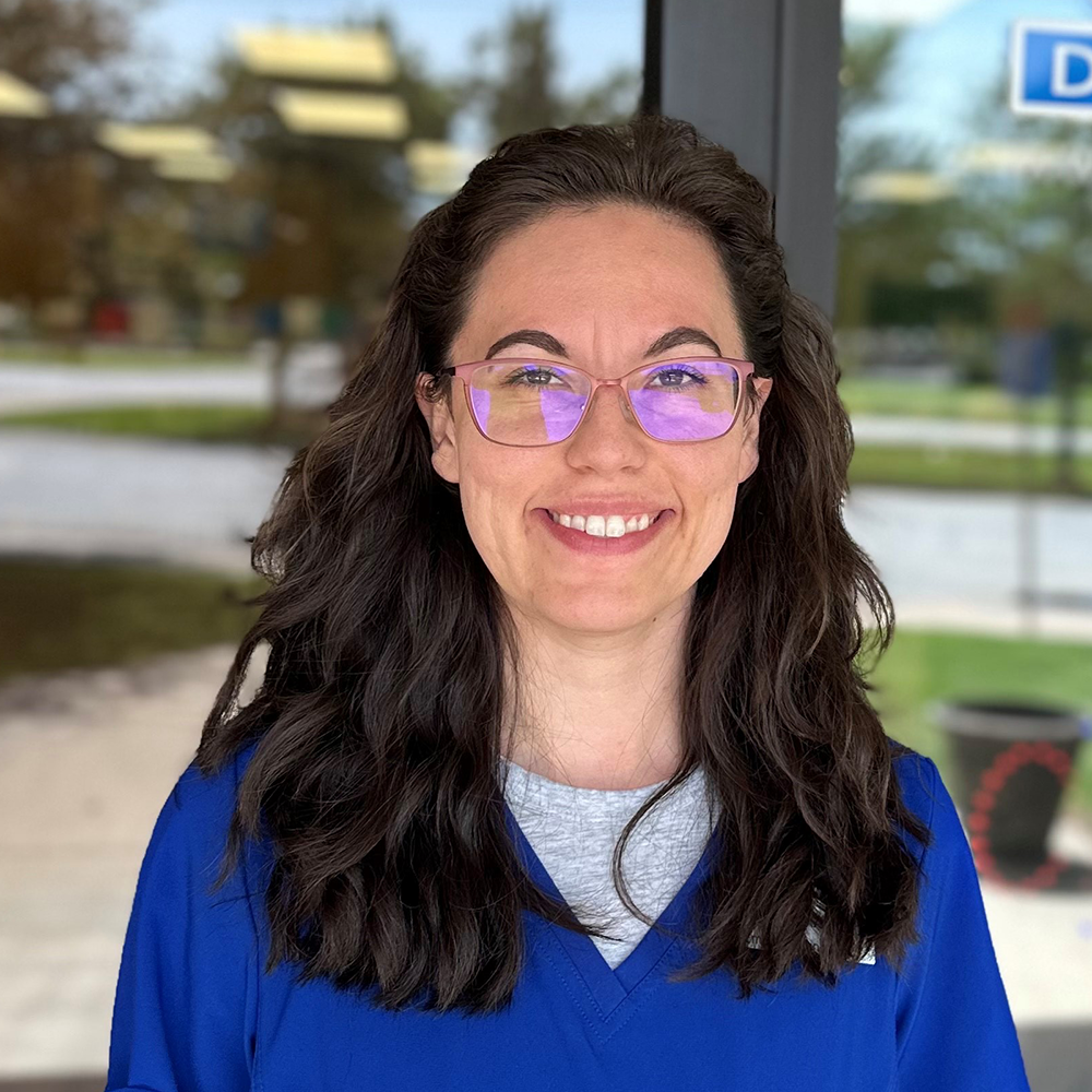 A man in a blue scrub is smiling in front of a pharmacy.