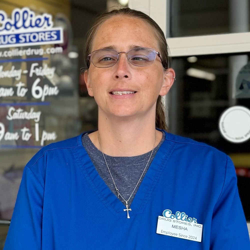 A man in a blue scrub is smiling in front of a pharmacy.