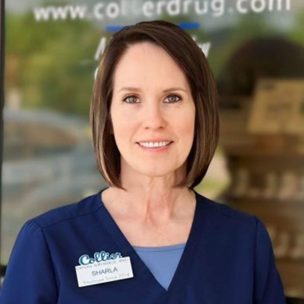 A young man wearing glasses and a blue scrub is standing in front of a pharmacy.