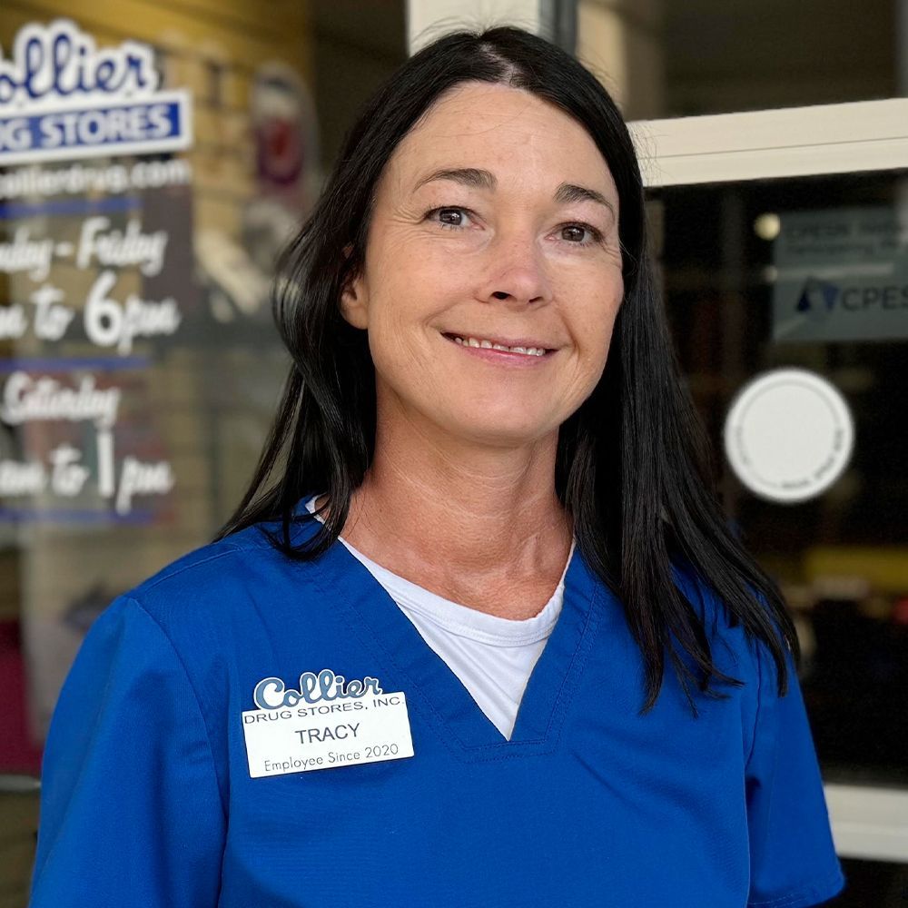 A young man wearing glasses and a blue scrub is standing in front of a pharmacy.