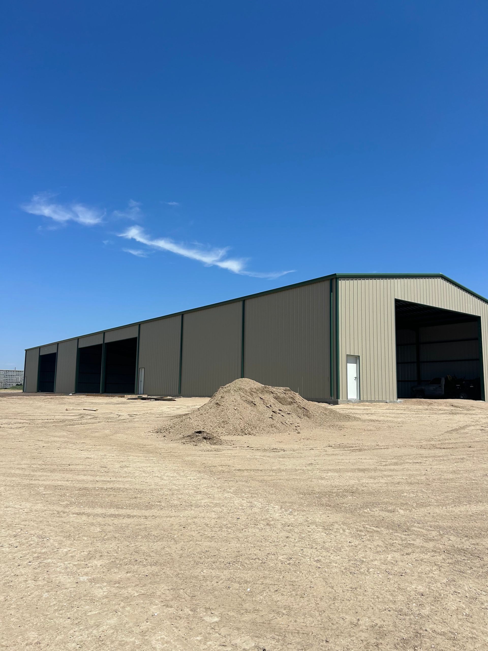 A large red building with a large door is in the middle of a dirt field.