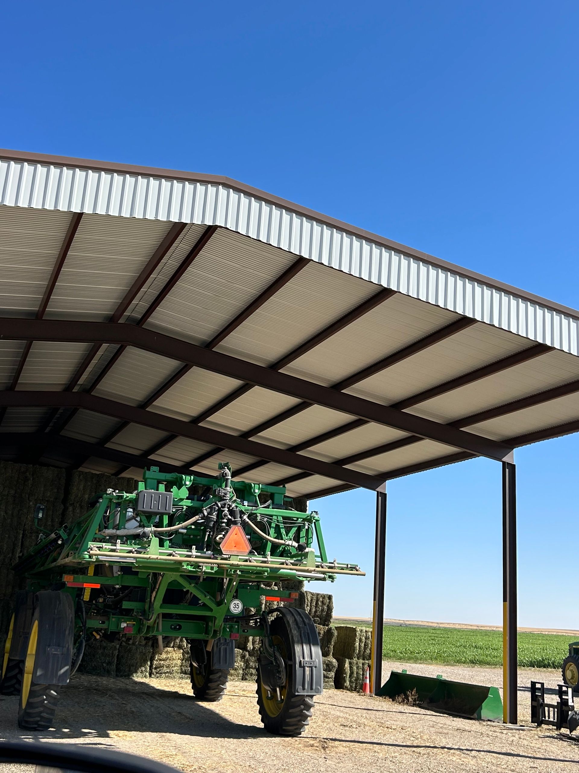 A green tractor is parked under a covered shed.