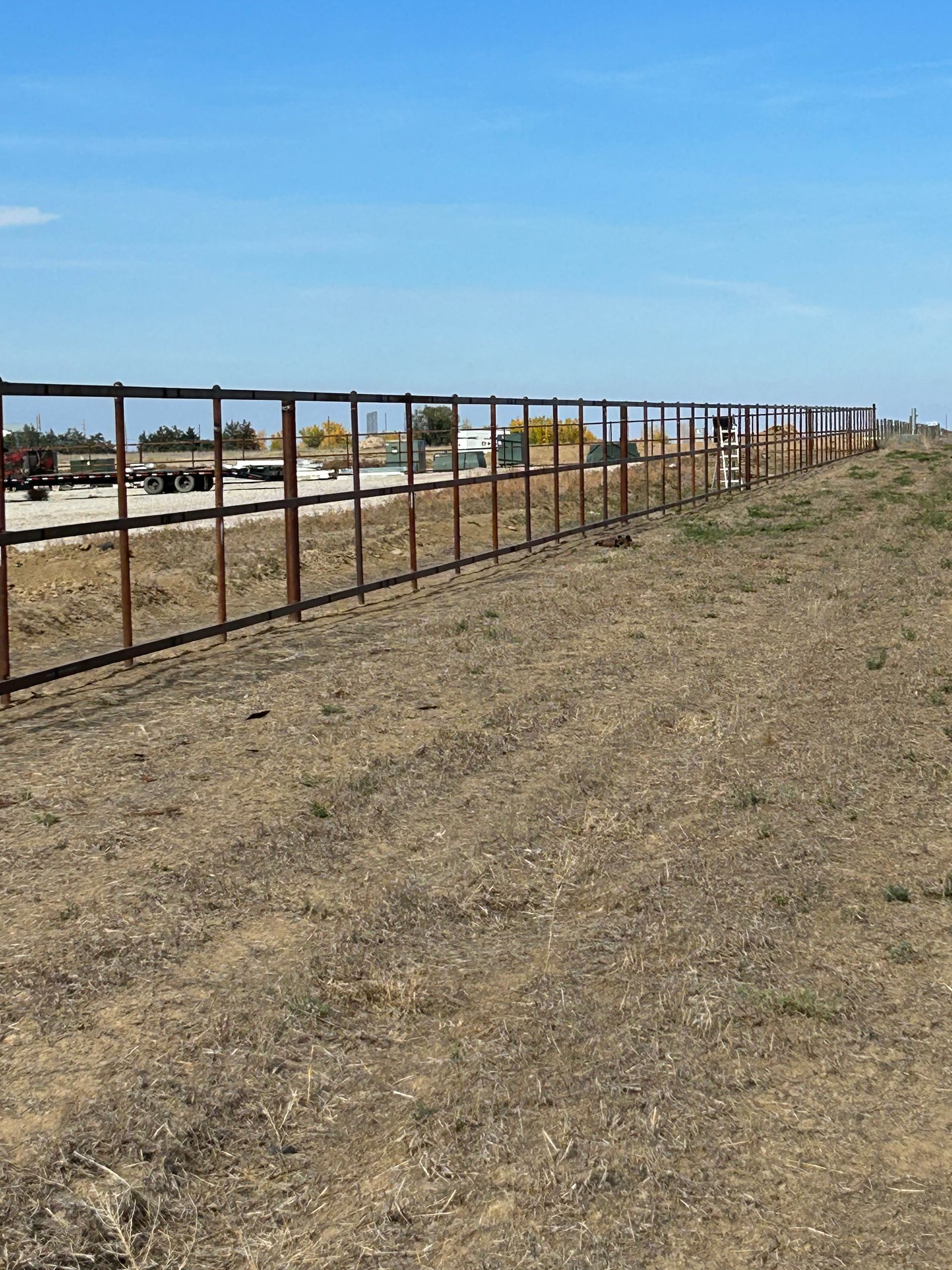 A long wooden fence surrounds a dry grass field.