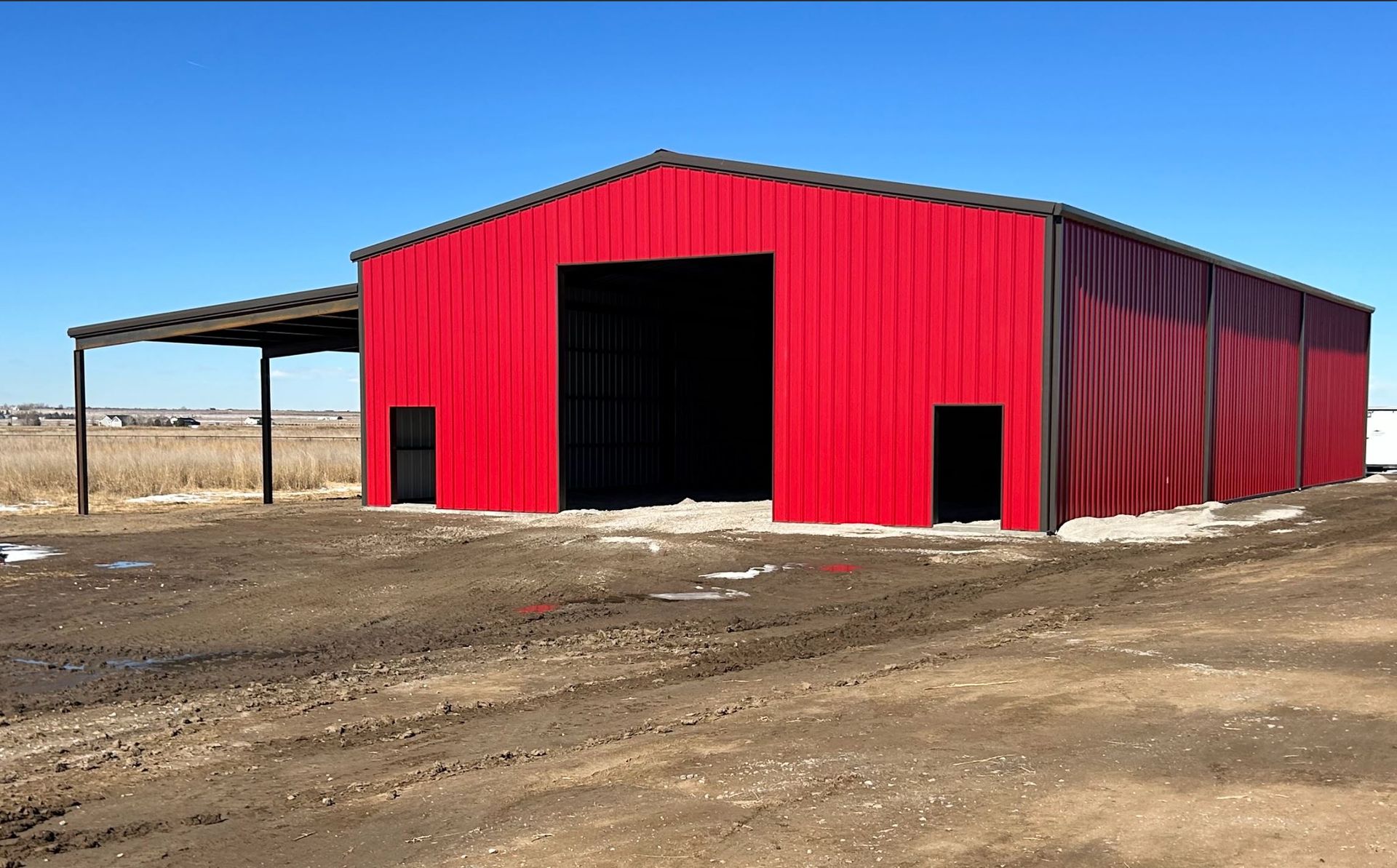 A large red building with a large door is in the middle of a dirt field.