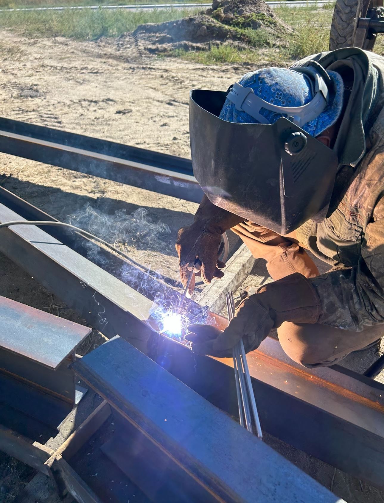 A man wearing a welding helmet is welding a piece of metal.