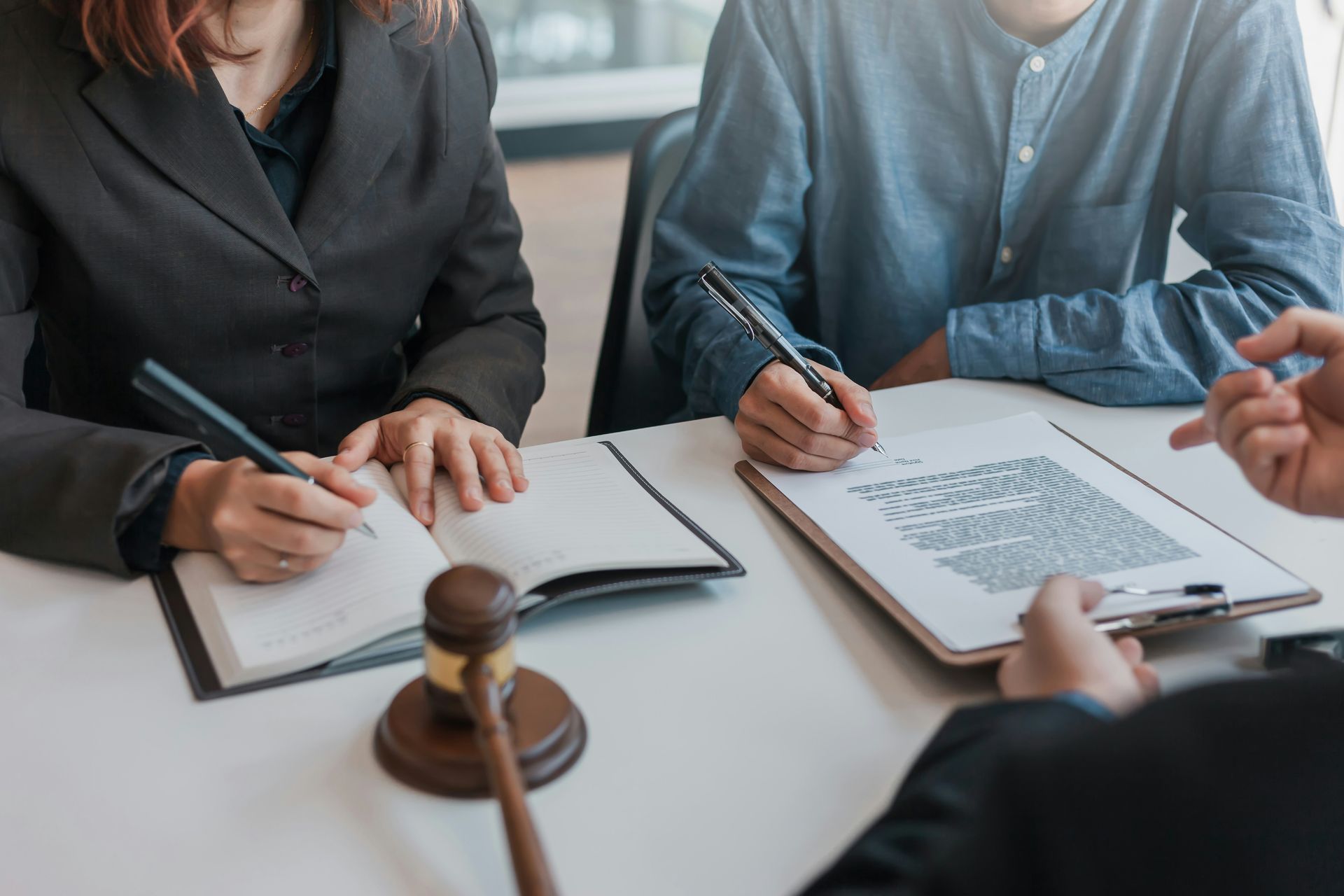 People signing documents at a table with a gavel, possibly in a legal setting.