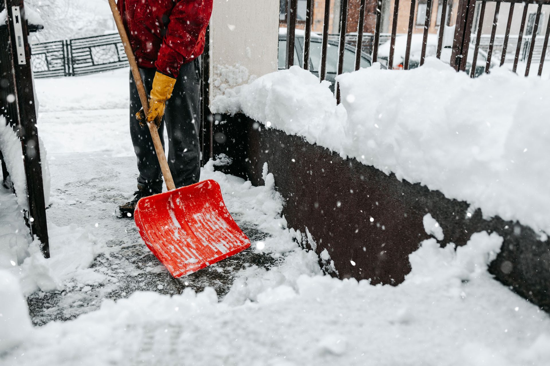 A person is shoveling snow from a sidewalk with a red shovel.
