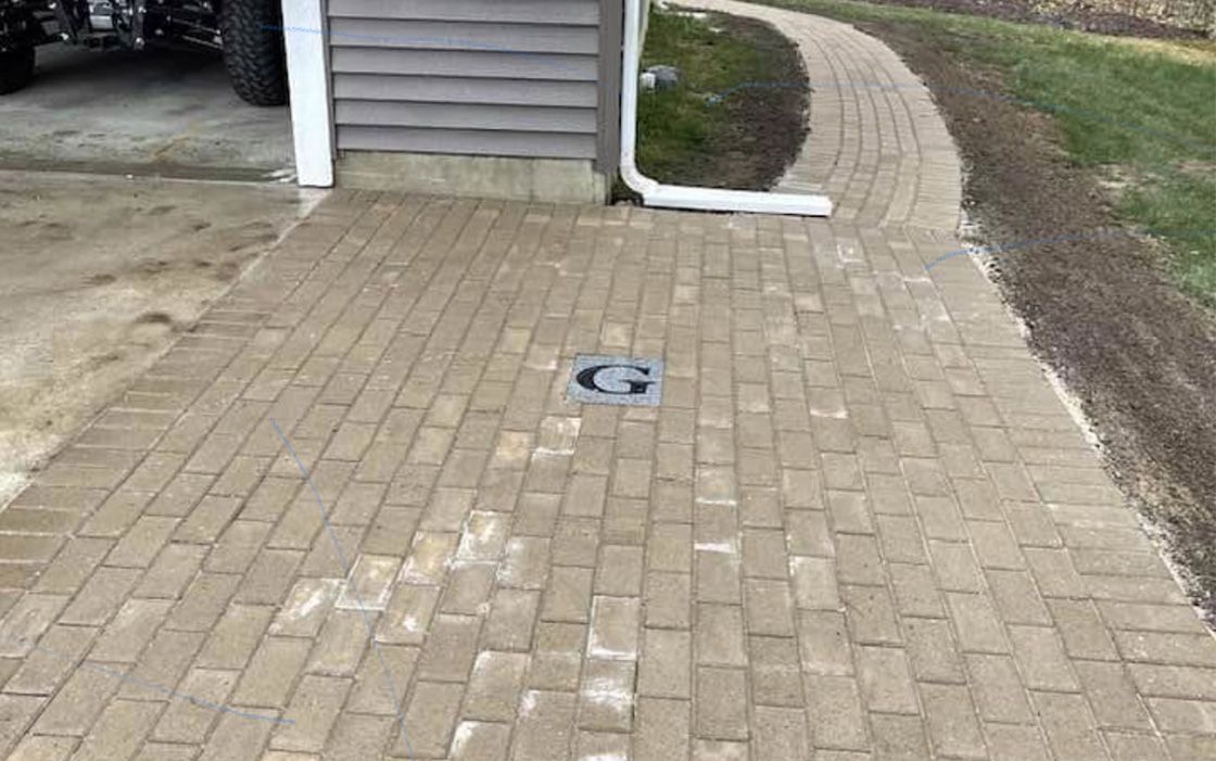 A brick walkway leading to a garage next to a house.