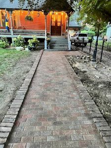 A brick walkway leading to a house with a porch.