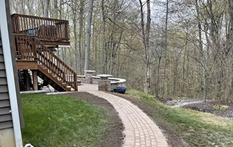 A brick walkway leading to a deck in the woods.