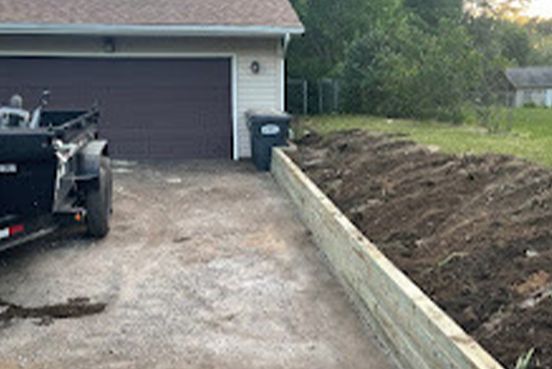A trailer is parked in front of a garage next to a wooden fence.
