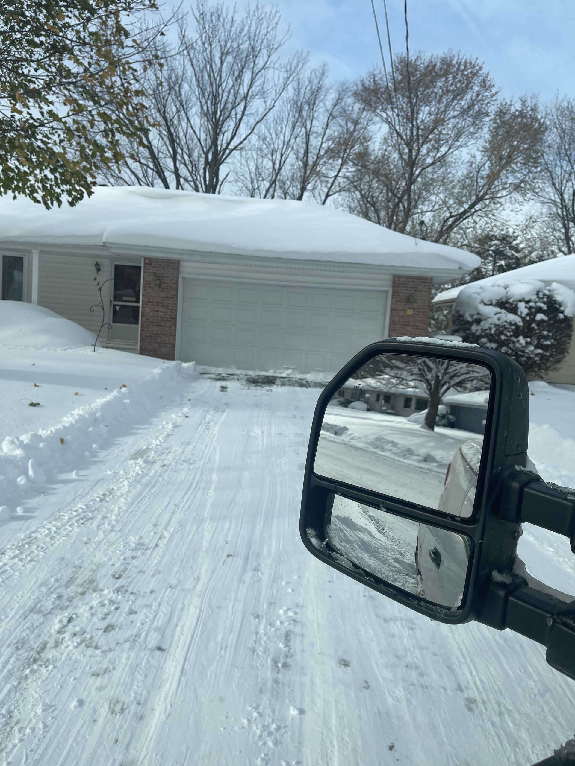 A car is driving down a snowy road in front of a house.