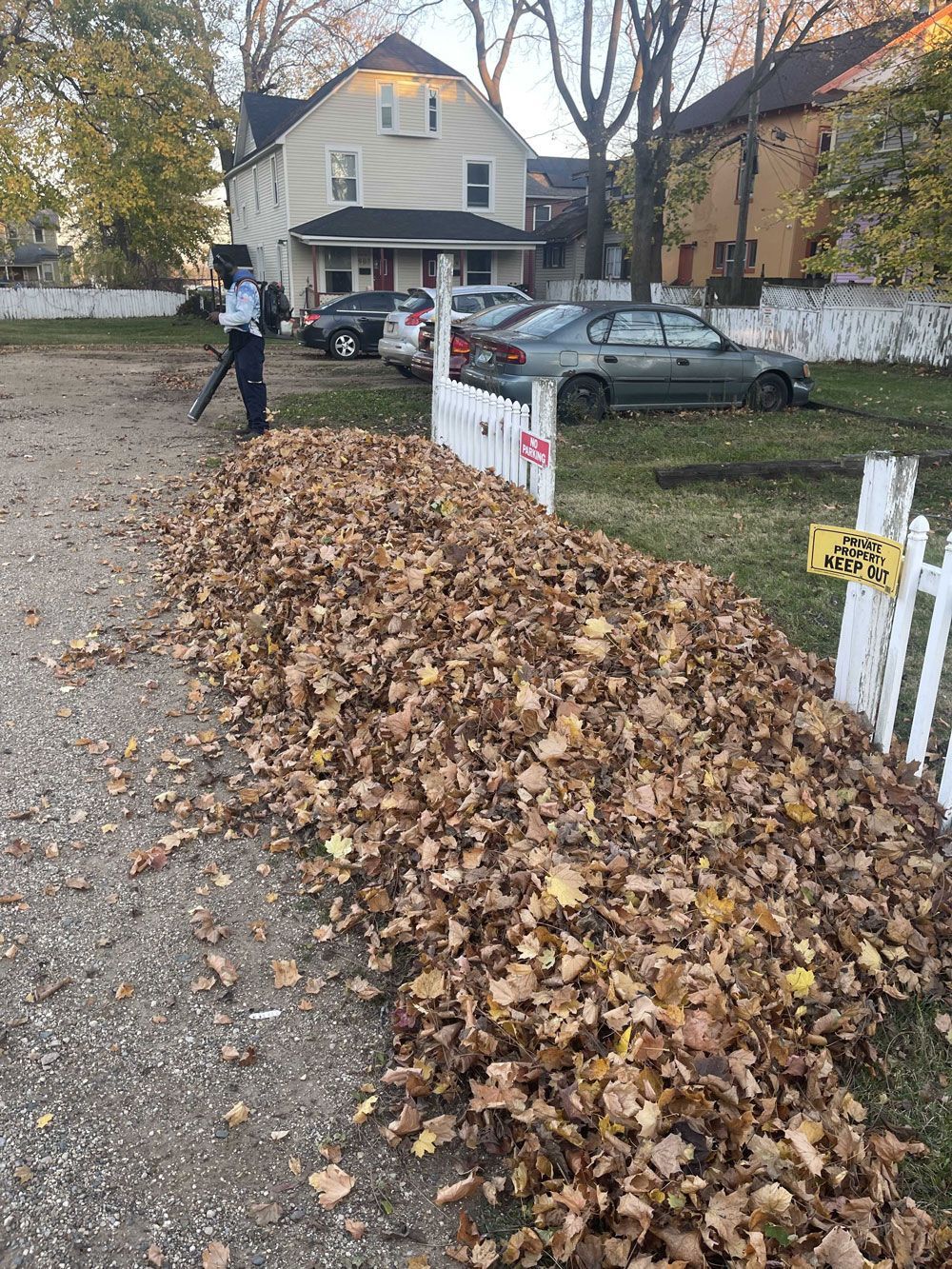 A person is blowing leaves on the side of the road.