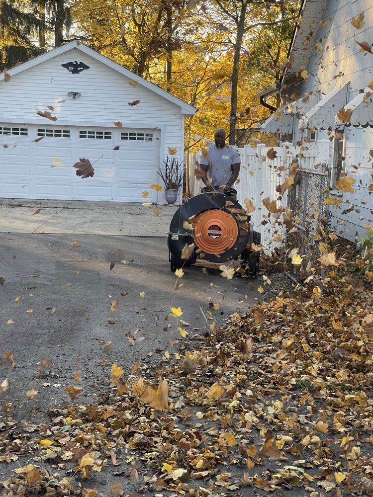 A man is using a leaf blower to blow leaves in front of a garage.