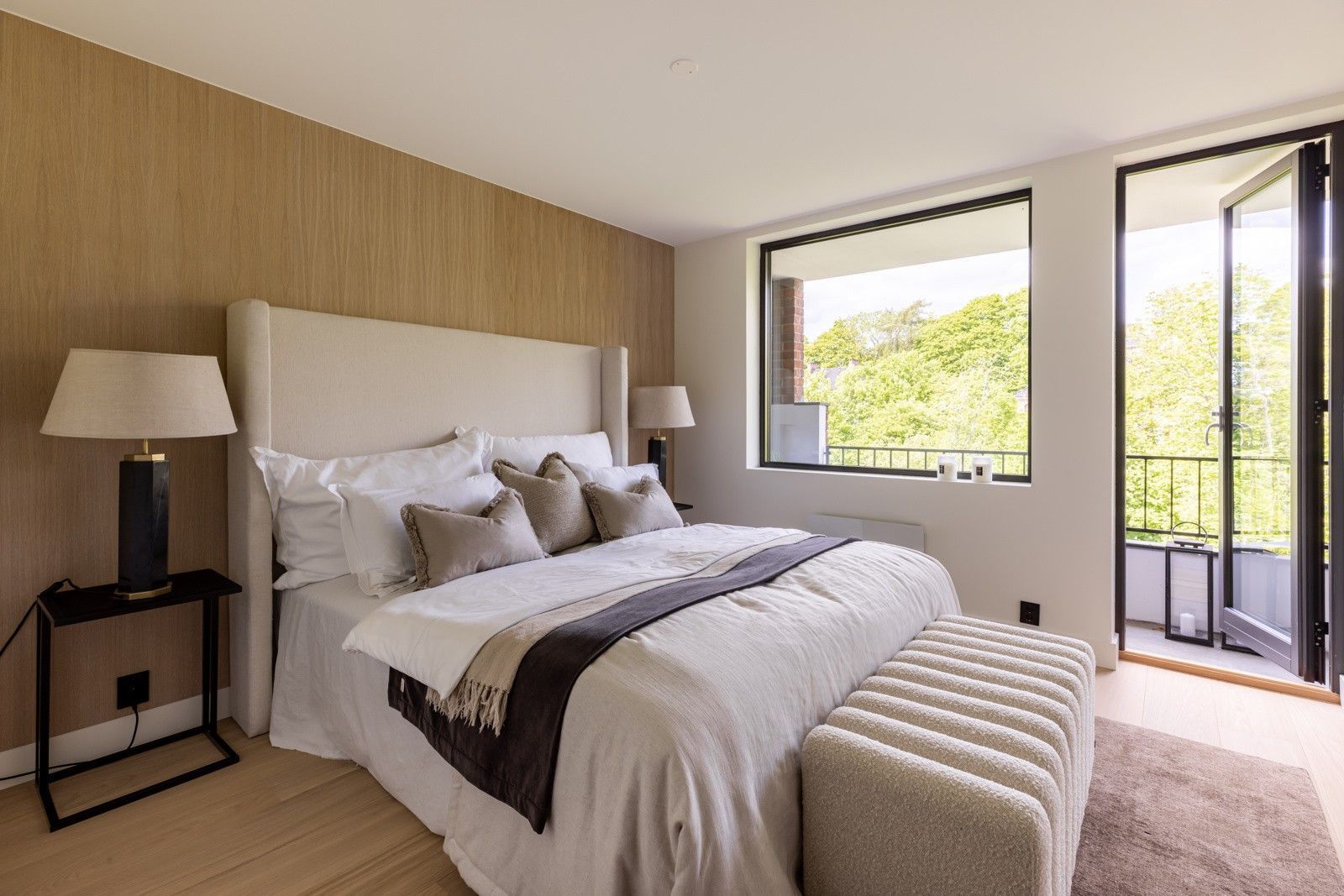 Et soverom med en stor seng, ottoman, lamper og en balkong.