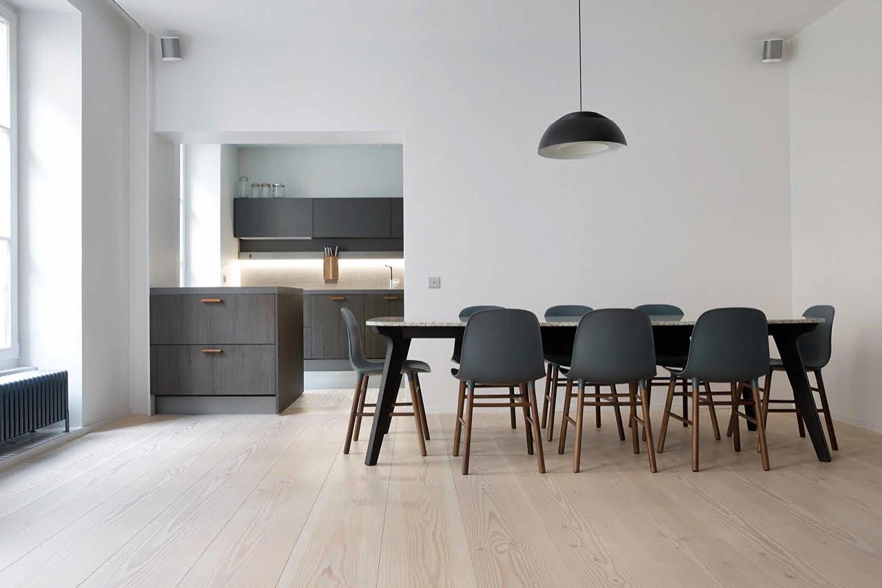En spisestue med bord og stoler og et kjøkken i bakgrunnen.