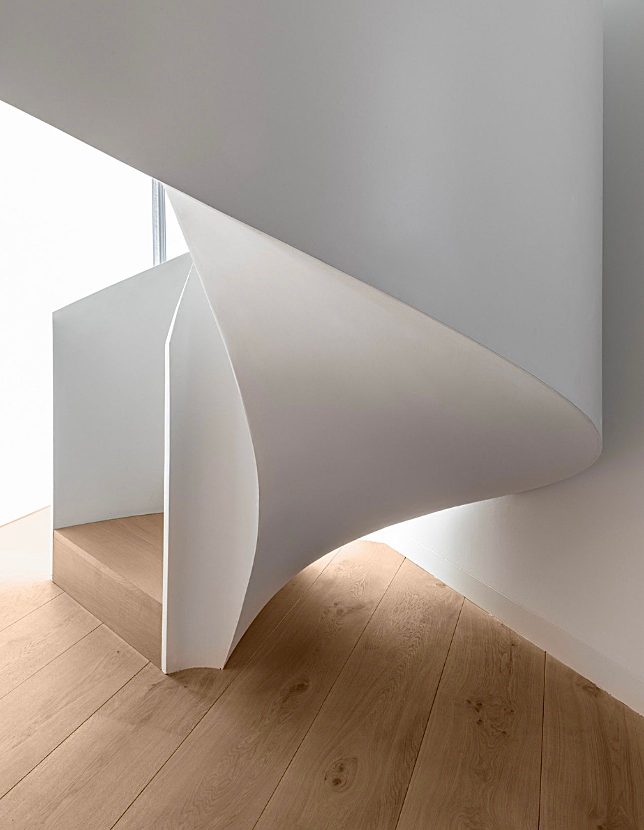 En spiraltrapp med tregulv og hvit vegg.