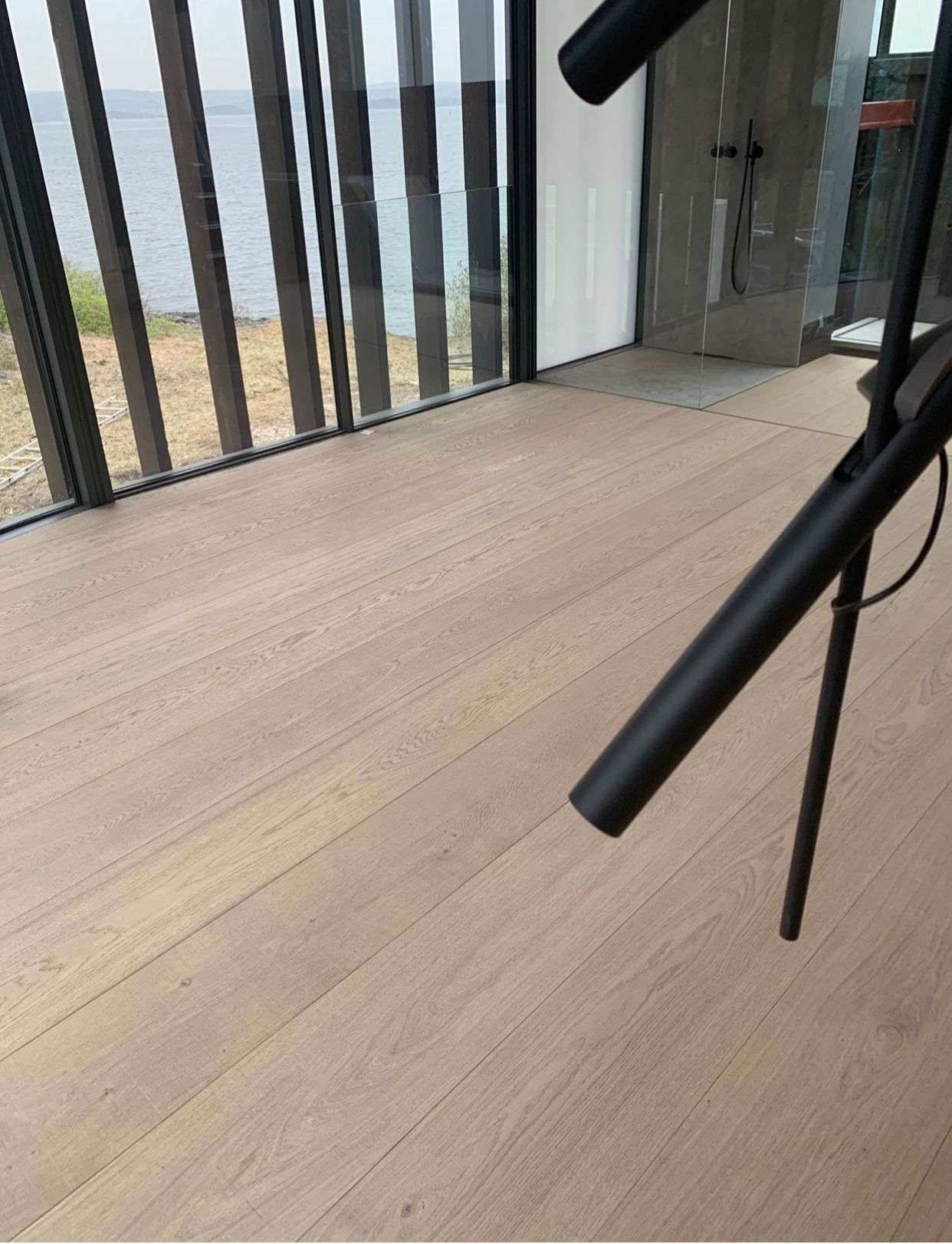 Et rom med tregulv og et stort vindu med utsikt over havet.