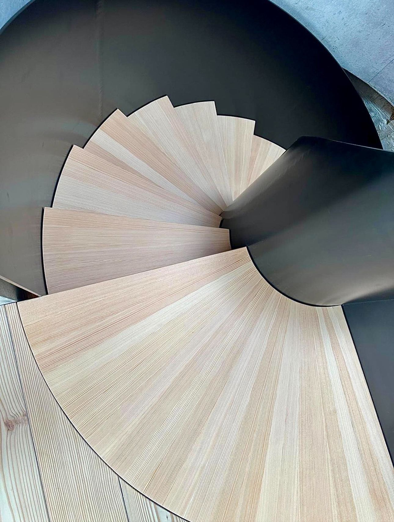 Et nærbilde av en trespiraltrapp med svart rekkverk.