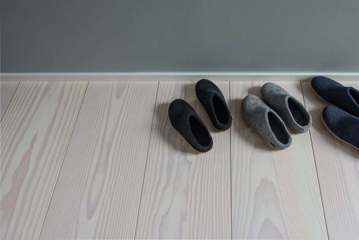 Tre par tøfler står på rekke og rad på et tregulv.