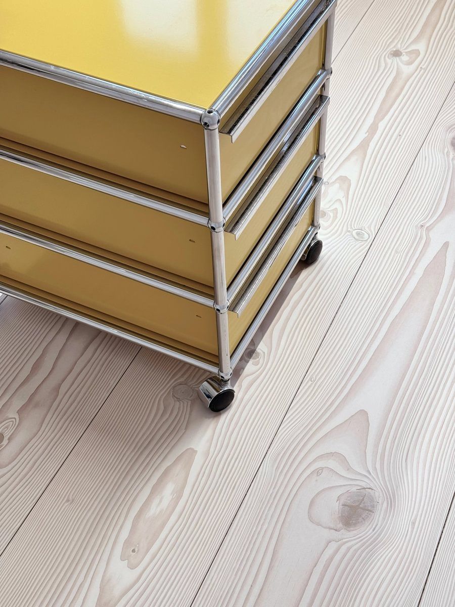 En gul skuff på hjul står på et tregulv