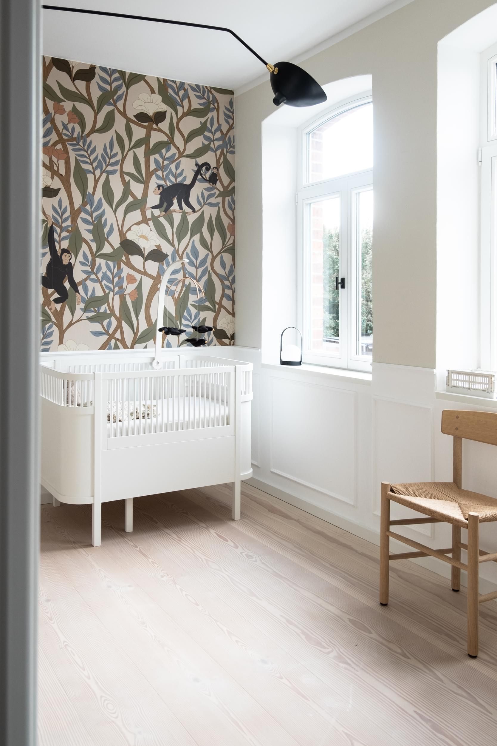 Et babyrom med barneseng, stol og vindu.