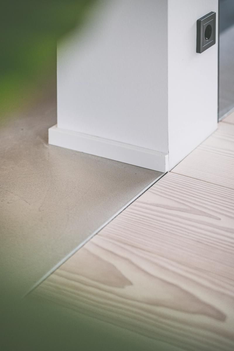 Et nærbilde av et tregulv med en hvit vegg i bakgrunnen.