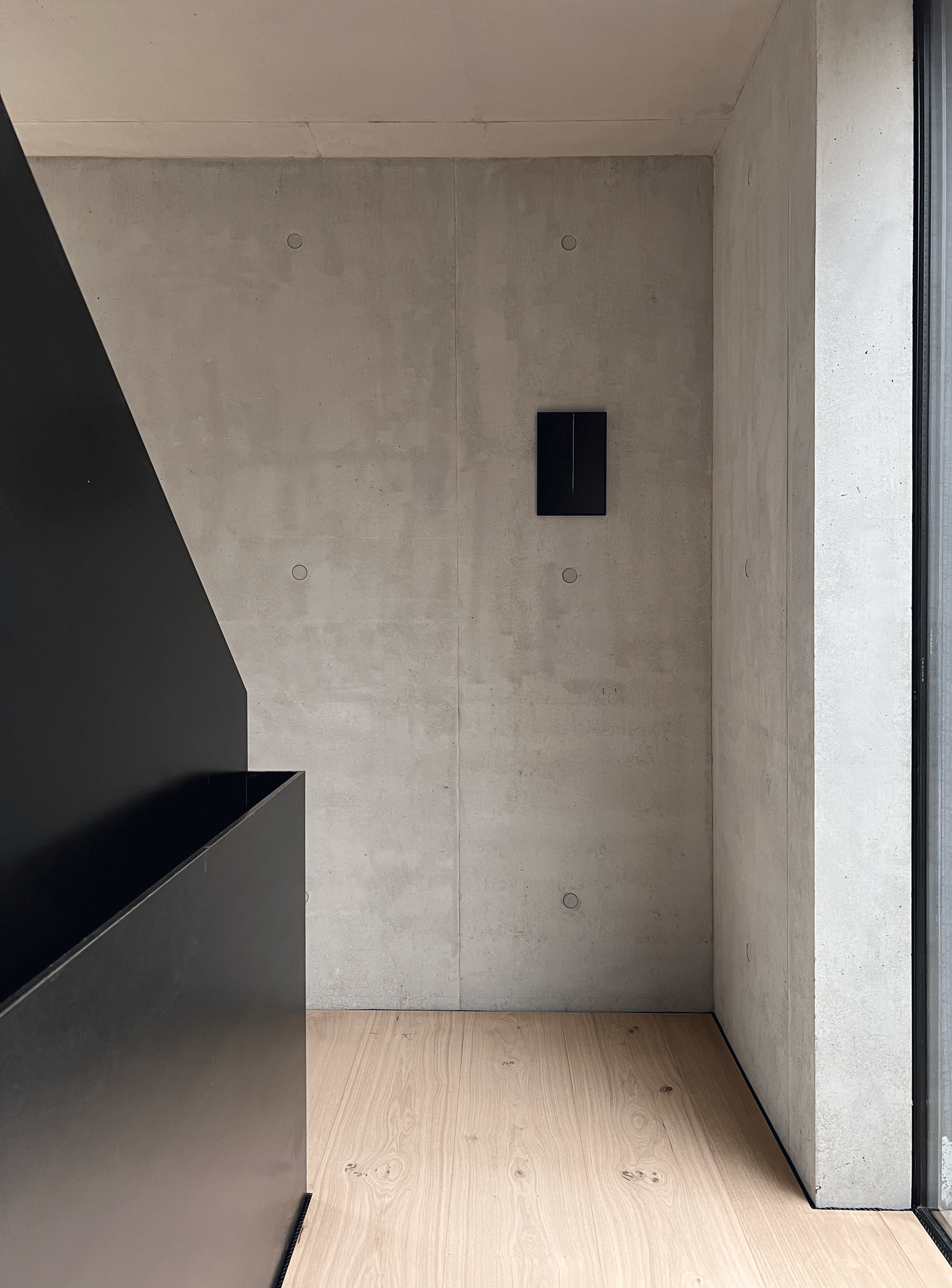 Et hjørne av et rom med betongvegg og tregulv.