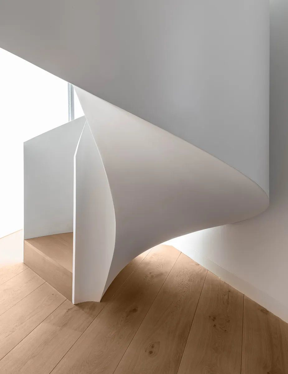 En spiraltrapp med tregulv og hvit vegg.