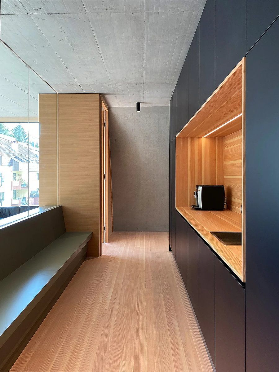 En lang gang med tregulv og sorte skap som leder til kjøkken.