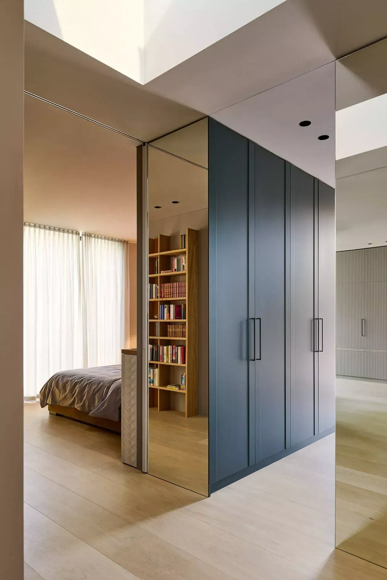 Et soverom med speildør som fører til en bokhylle og en seng.