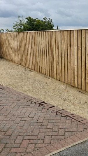 A wooden fence is sitting next to a brick driveway.