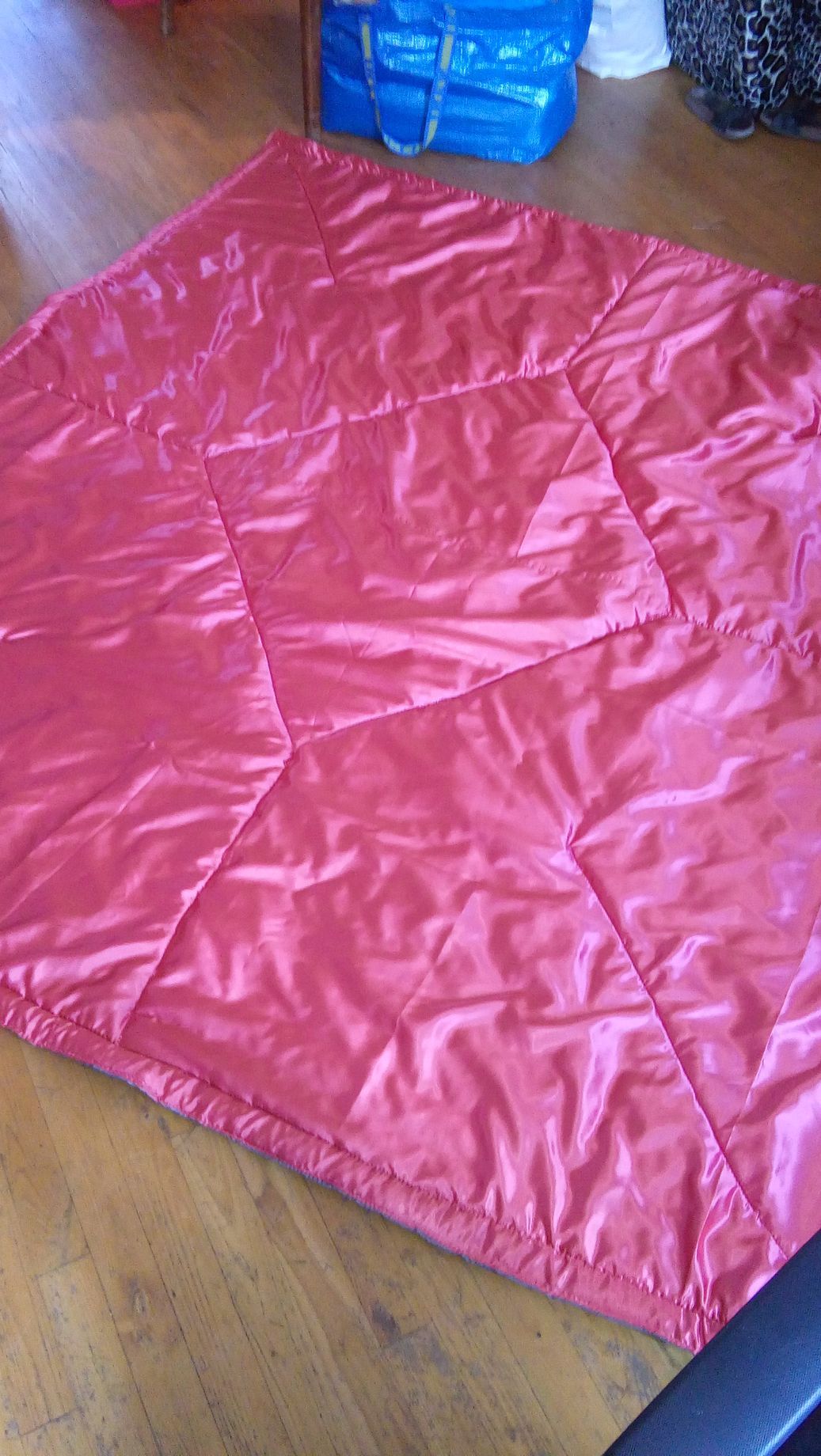 Une couverture rouge est posée sur un plancher en bois à côté d'un sac bleu.