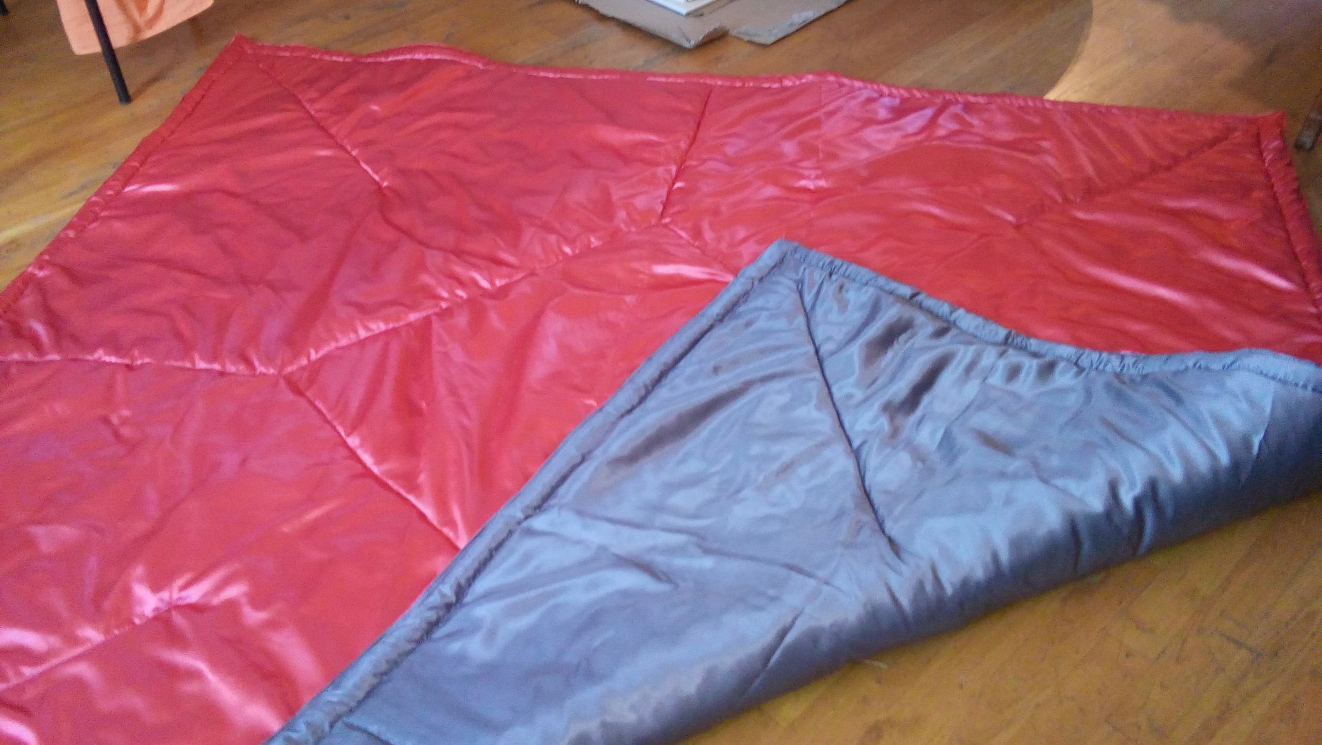 Une couverture rouge et grise est posée sur un parquet.