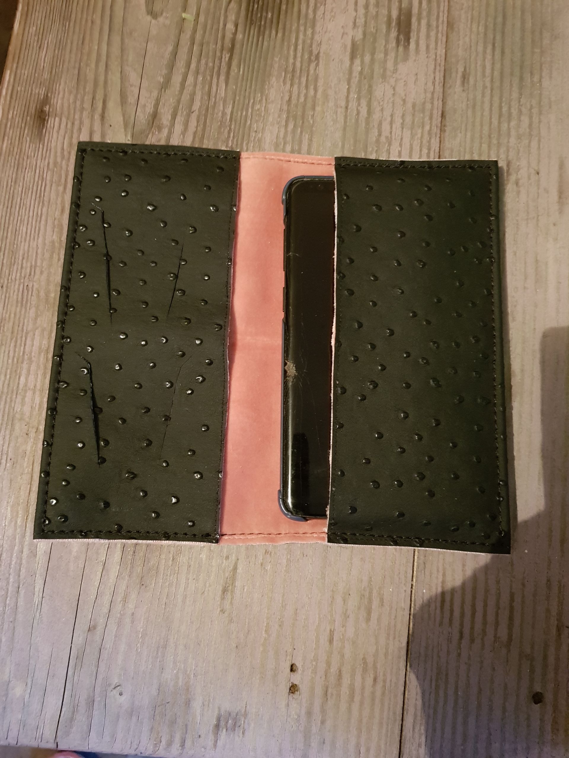 Un téléphone portable se trouve à l’intérieur d’un portefeuille sur une table en bois.