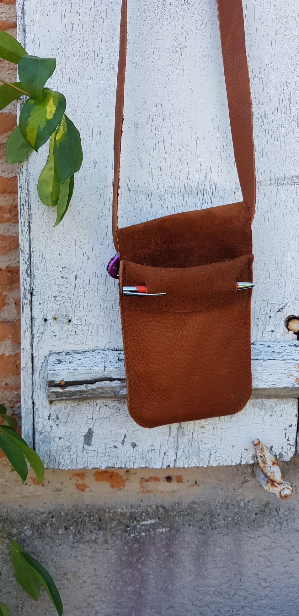 Un sac à main marron avec une longue sangle est accroché sur un mur blanc.
