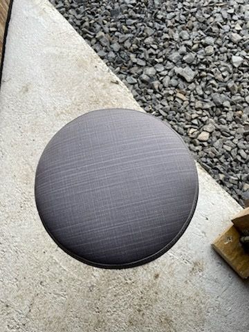 Un tabouret rond repose sur le sol à côté d’un tas de pierres.