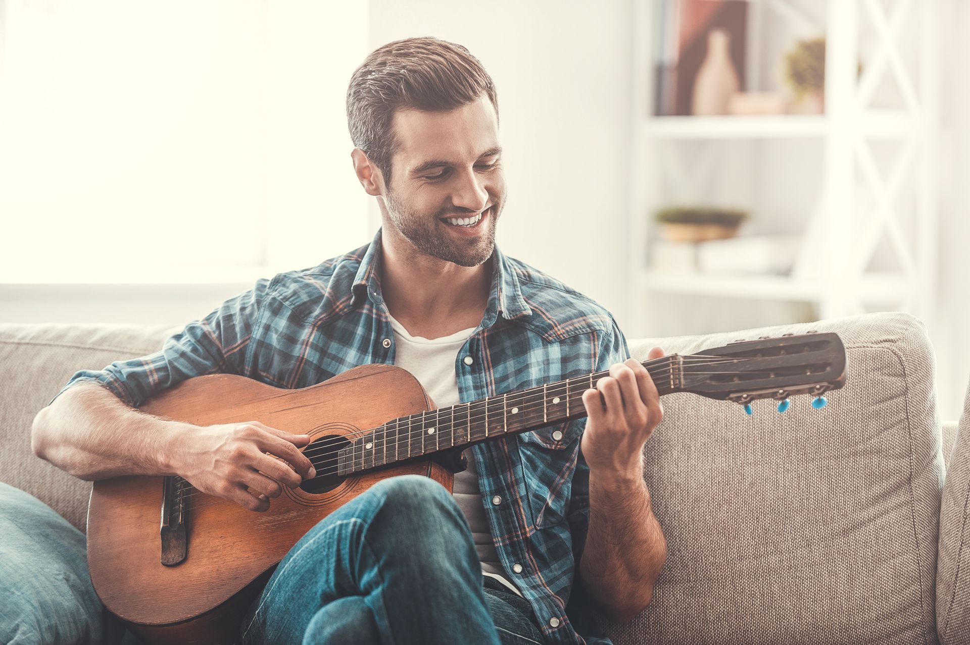a man is sitting on a couch playing an acoustic guitar .