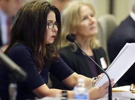 A woman is sitting at a table holding a piece of paper in front of a microphone.
