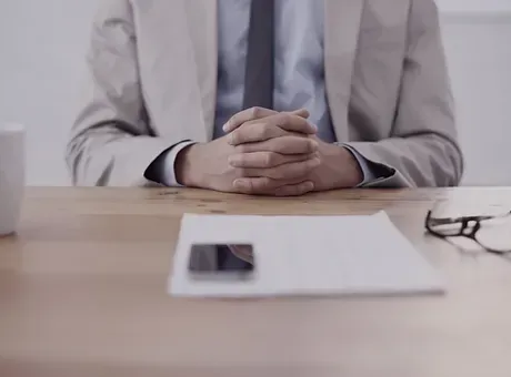 A man in a suit and tie is sitting at a table with his hands folded.