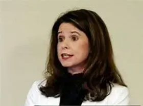 A woman with long brown hair is wearing a white jacket and a black shirt.