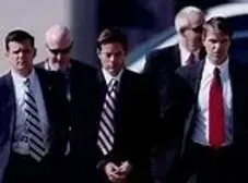 A group of men in suits and ties are walking down a street.